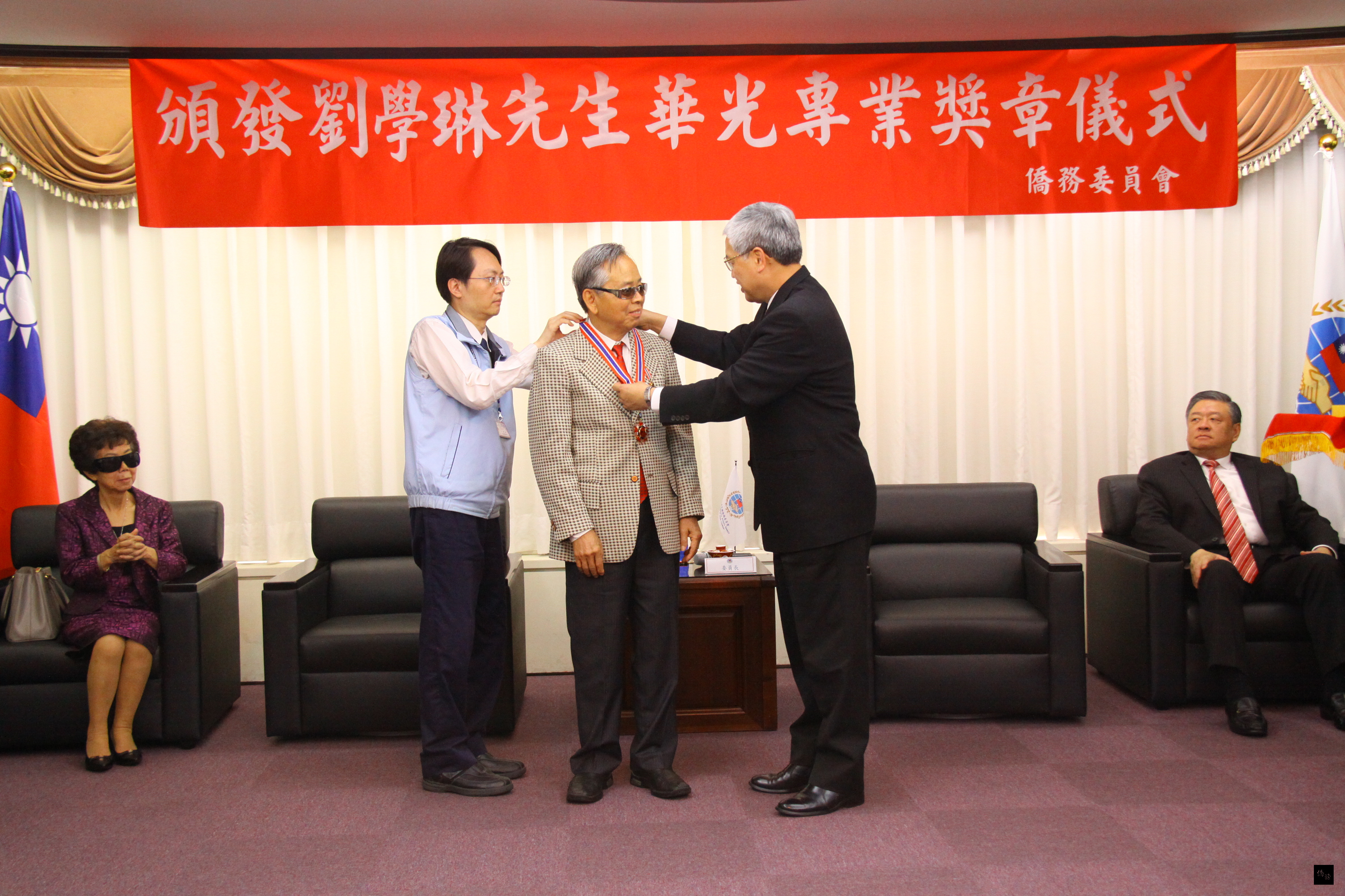僑務委員會委員長陳士魁(右)為僑務諮詢委員劉學琳(中)戴上華光專業獎章。