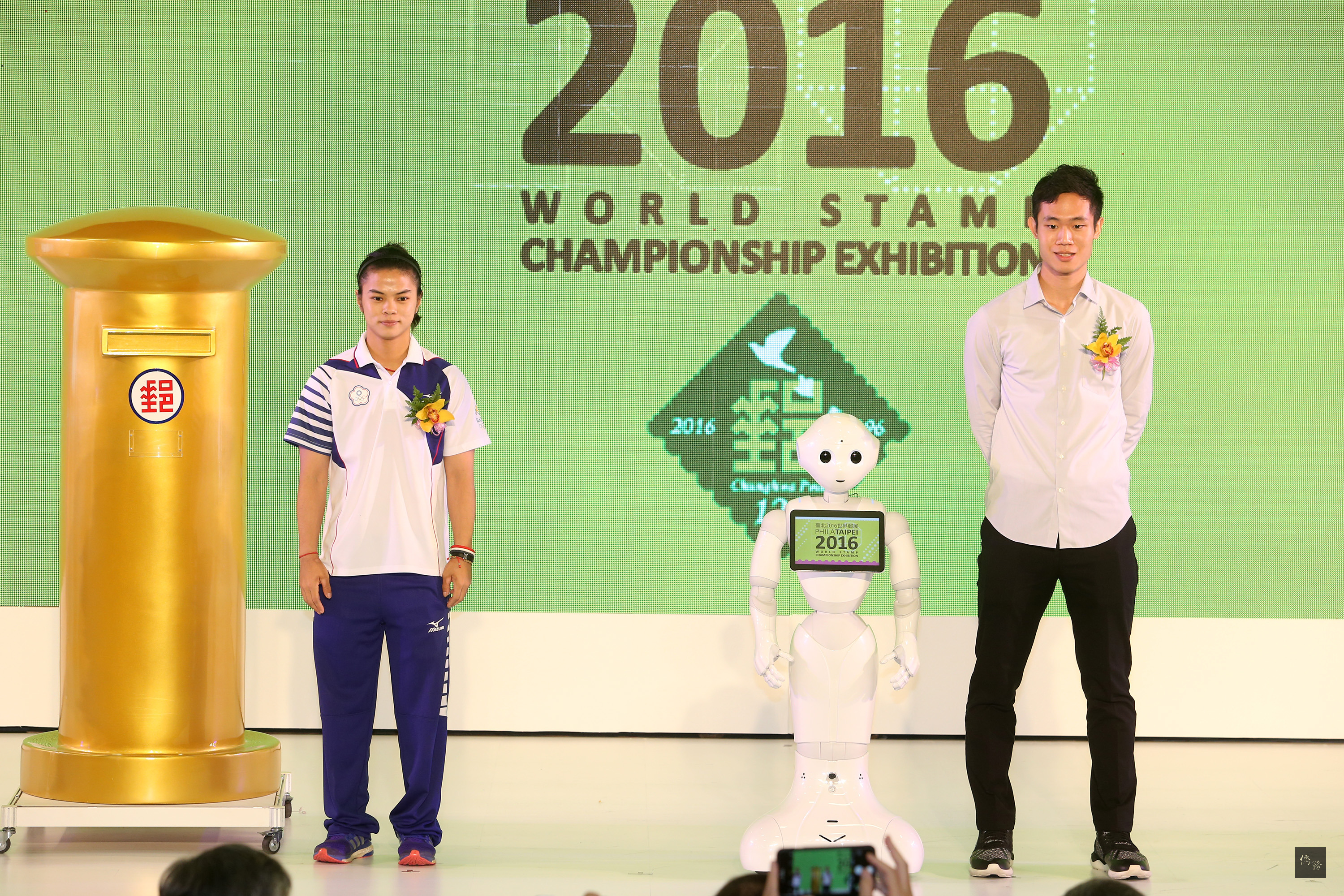 台灣首次舉辦的「2016世界郵展」21日起連續6天在台北世貿一館展出,機器人PEPPER(中)在開幕儀式中,與奧運金牌選手許淑淨(左)、教練蔡溫義、獲邀擔任郵政大使的台灣羽球選手呂家弘(右)及中華郵政為許淑淨家鄉打造的金色郵筒共同現身。(中央社提供)