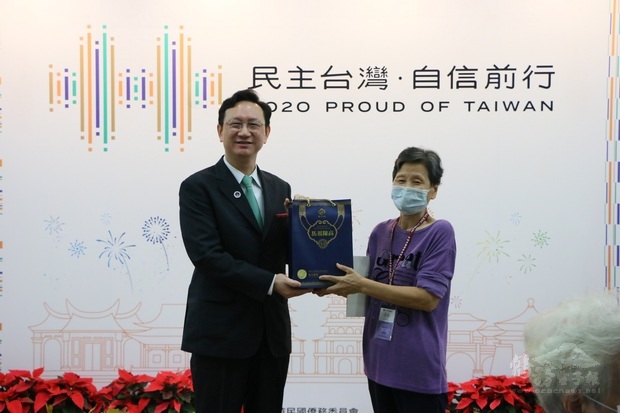 僑委會委員長童振源(左)致贈紀念禮品予首位報到僑胞陳羽莎(右)。