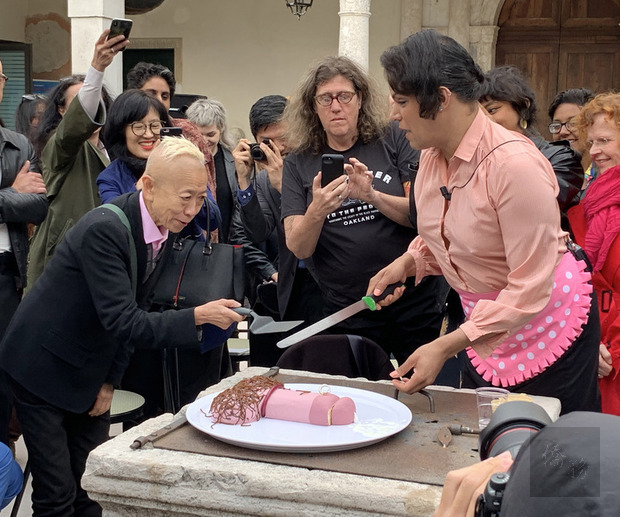 威尼斯雙年展台灣館11日舉辦酷兒主題的公共論壇，演員請藝術家鄭淑麗（左）品嚐陽具造型蛋糕，象徵展覽打破傳統性別思維。（中央社提供）