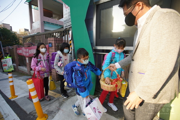 台北市中、小學22日開學，桃源國小校長張鍾榮（右）
在校門口與學生互道「新年快樂」，發糖果歡迎學生。