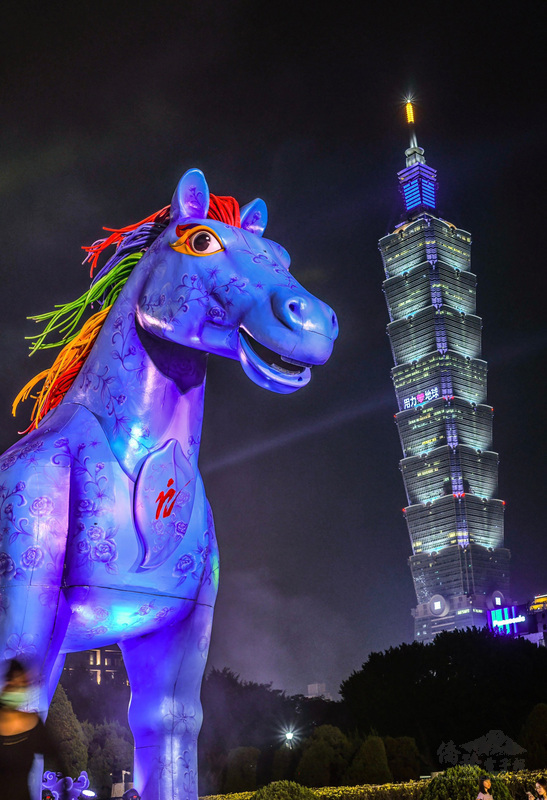 紙風車客家親子劇「雨馬」前進台北國父紀念館，高達10公尺高的巨型道具「雨馬」格外吸睛；27日晚間「雨馬」與台北101大樓同框，搭配點頭、噴煙與一旁噴水池水舞，就像一場燦爛的燈火嘉年華。（紙風車劇團提供）
