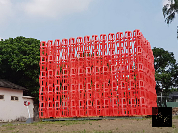 屏東地景藝術節10月起在屏東市勝利新村登場,10座大型裝置藝術豎立或隱藏在眷村的街角巷弄。圖為裝置藝術作品之一「放空洞」,大量紅色塑膠板凳椅組成。(中央社提供)