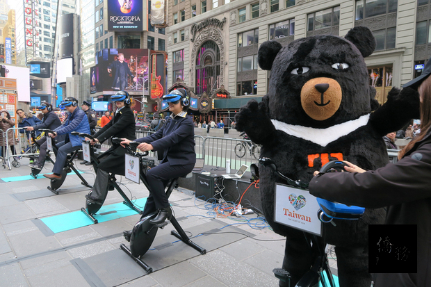 觀光局駐紐約辦事處7日在時報廣場擺攤，以虛擬實境（VR）健身自行車讓紐約客「穿越時空」到台灣，台灣觀光大使「喔熊組長」也出席同樂。(中央社提供)
