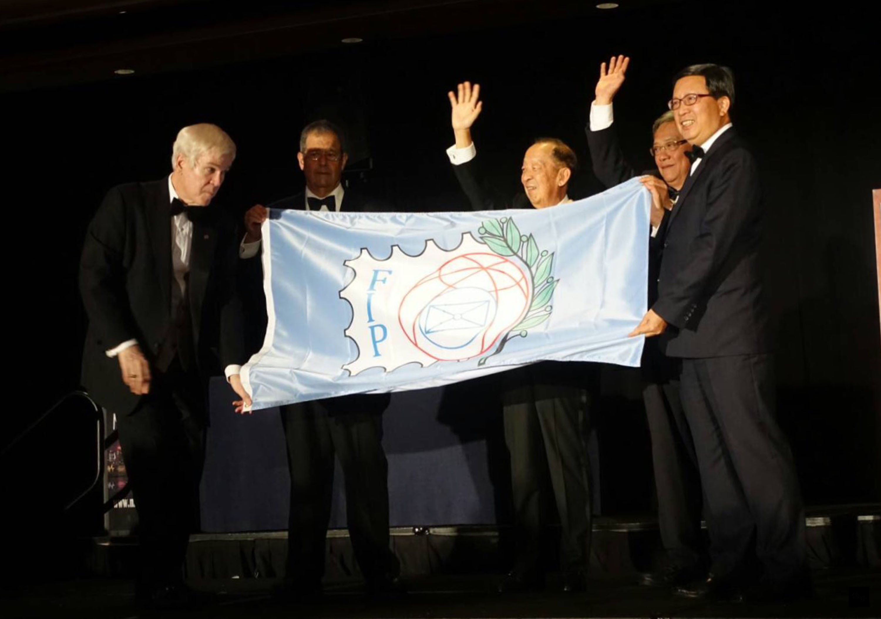 中華郵政董事長翁文祺(右)2日從2016紐約世界郵展主席沙迪、國際集郵聯合會會長鄭炳賢(中)手中接下FIP會旗,這是世界郵展首度在台舉辦,也是中華郵政120年來頭一遭。(中央社提供)