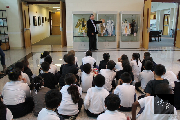 學生們在文化導覽志工老師盧瑞平的帶領下參觀中心大廳陳列的布袋戲偶。(華府僑教中心提供)