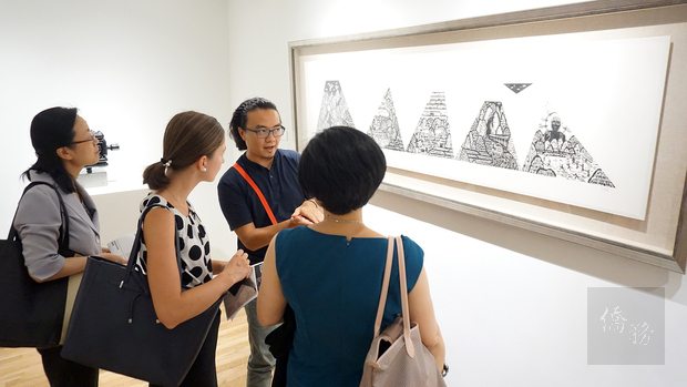 蔡坤霖向參觀當地藝術愛好者與僑胞介紹其版畫作品《秋吉台行旅圖》。