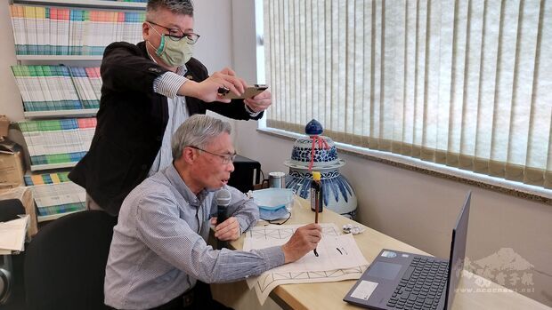 廖世秉(坐者)在鏡頭前示範楷書的寫法。