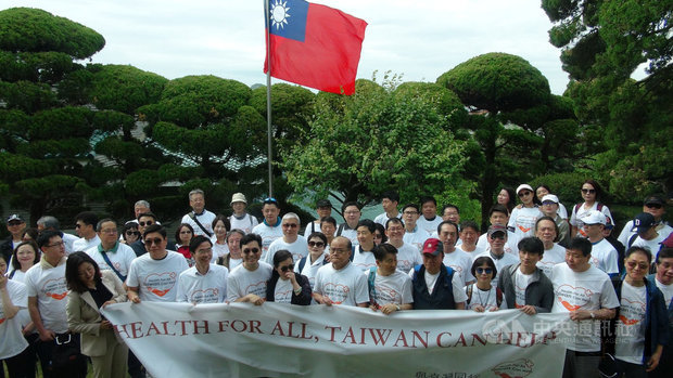 唐殿文（前左4）、趙慶泰（前左3）、李寶禮（前左6）18日在首爾平昌洞代表官邸手持印有「Health for all, Taiwan can help」布條，在國旗前為支持臺灣參與世界衛生大會展開健走。（中央社提供）