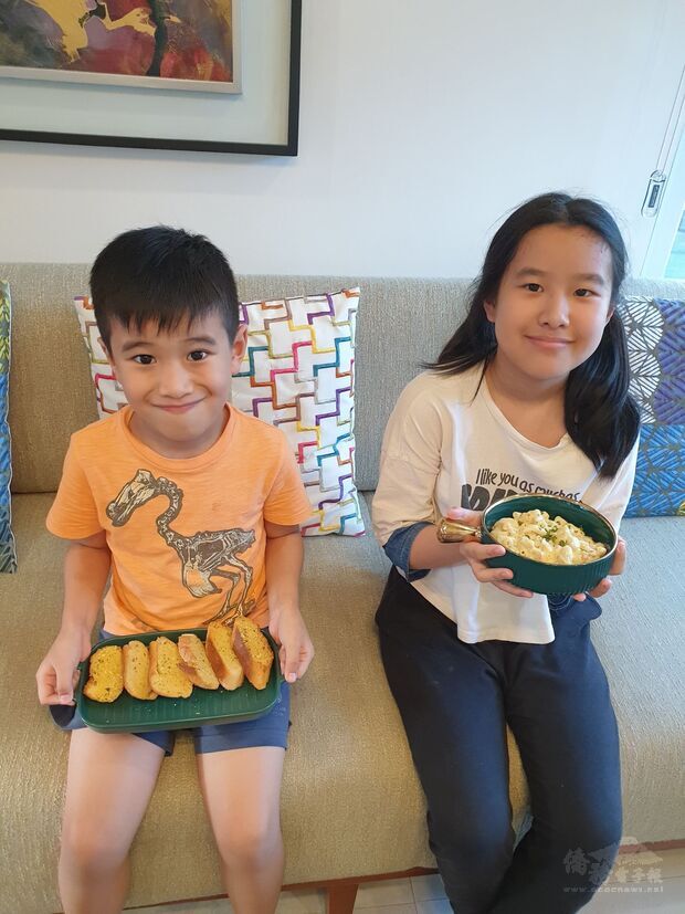 菲華文經總會兒童線上烹飪班學員鍾鈺明(左)與鍾雪真(右)展示烹煮好的芝士通心粉與大蒜麵包。