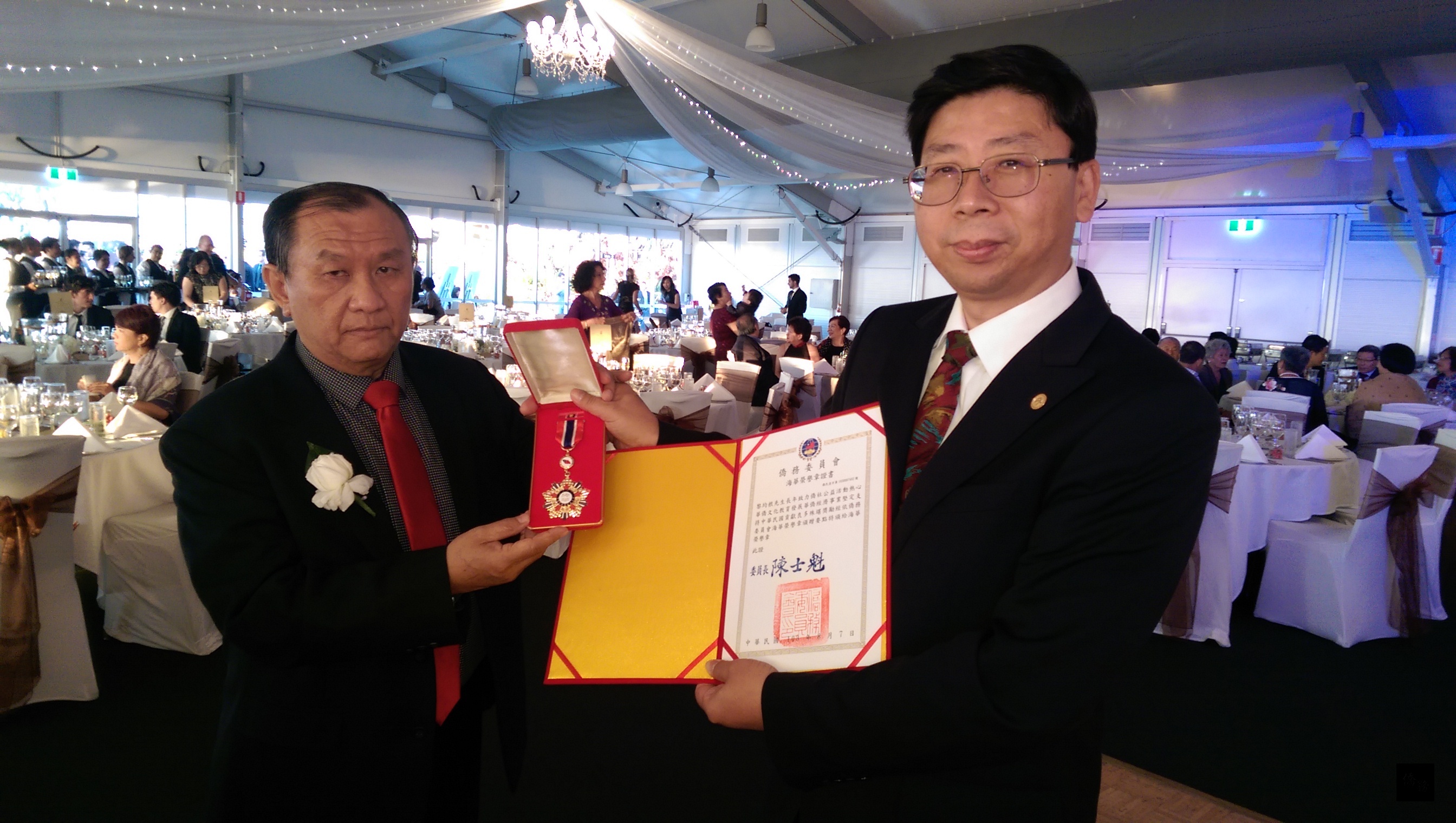 駐布里斯本辦事處處長賴維中(右)代表頒發僑委會海華榮譽章及證書給黎均根,其子黎國偉僑務顧問(左)代表受贈。(布里斯本僑教中心提供)