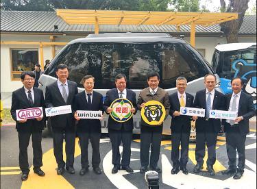 Lin Chia-lung, center right, Cheng Wen-tsan, center left, and other officials, stand in front of an autonomous bus, holding placards with the logos of organizations sponsoring trials of driverless vehicles at a news conference in Taoyuan yesterday. /