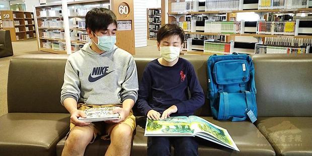 Wu Ching-yu, right, accompanied by his father, reads a book at the Kaohsiung Main Public Library on Friday. / Photo courtesy of Taipei Times