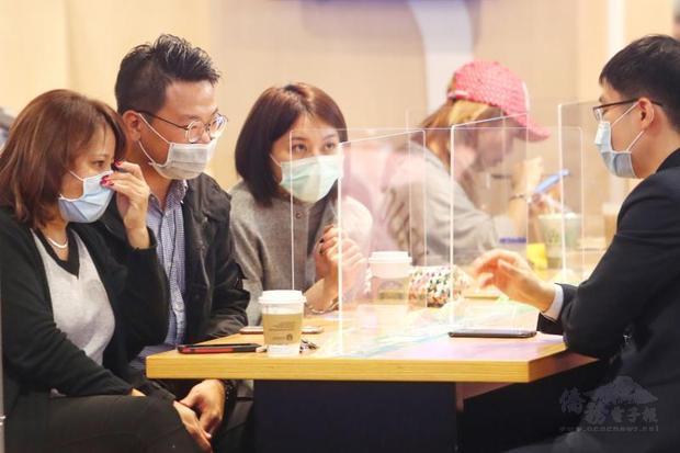 People wearing masks talk across transparent plastic partitions as a precaution against the spread of COVID-19 in Taipei yesterday./Photo courtesy of CNA