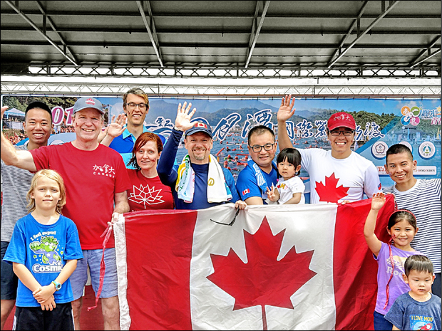 加拿大駐台代表芮喬丹（中，藍帽）成功挑戰日月潭泳渡，上岸後開心與隊友拿著國旗合影。（自由時報提供）