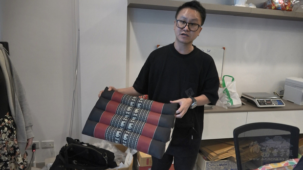 台灣人鄭鈞元在曼谷經營旅行社,因為武漢肺炎疫情影響,業績受重創,公司決定改做代購。圖為鄭鈞元手拿著台灣人喜愛的泰國紀念品三角枕。(中央社提供)