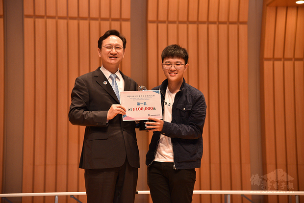 黃崇理從僑務委員會委員長手中接到獎座與獎金。